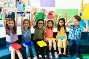 Cheerful preschool children raising their hands and having fun while learning in kindergarten